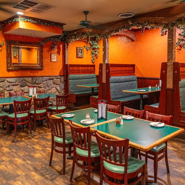 Interior of Marri's Pizza & Pasta, featuring green tables, wooden chairs, booths, and orange walls with ivy.
