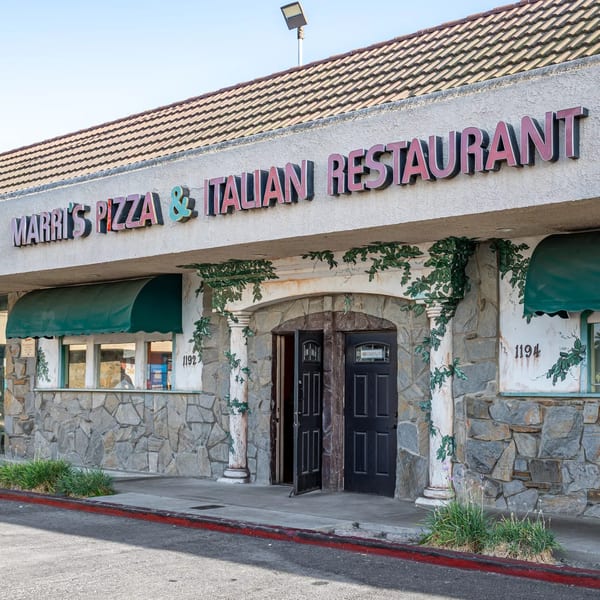 Exterior of Marri's Pizza & Italian Restaurant with stone facade, green awnings, and ivy details.