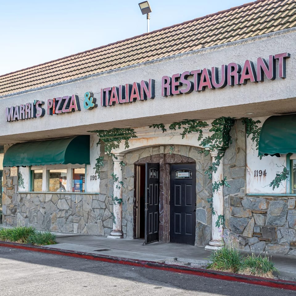 Exterior of Marri's Pizza & Italian Restaurant with stone facade, green awnings, and ivy details.