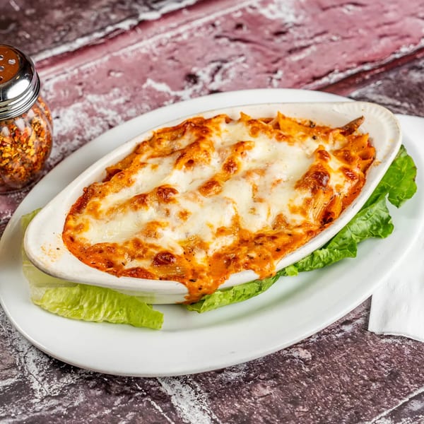 Baked ziti with melted cheese and red sauce in a white dish, with a shaker of red pepper flakes.