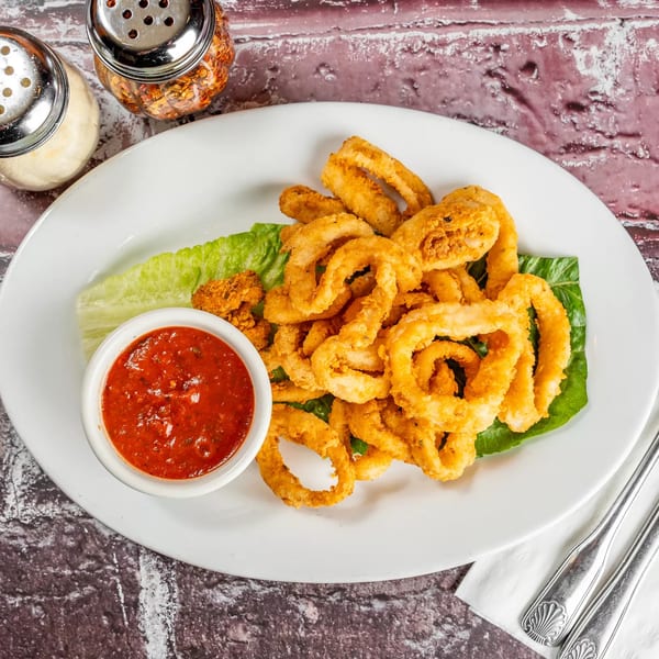 Crispy fried calamari rings on lettuce with a side of red marinara sauce, parmesan, and chili flakes.