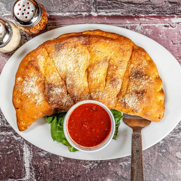 A golden-brown calzone with parmesan cheese, a side of marinara sauce, and a pizza server.